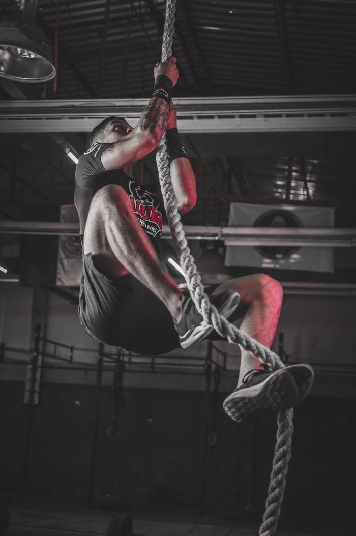 our-services-3 A determined man climbing a rope in an indoor gym setting, showcasing strength and fitness.